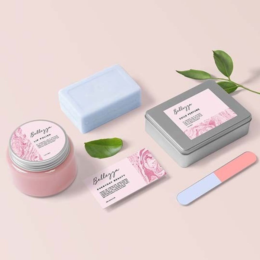 wp kozmetika okrogla 1-5in bela folija Na sliki so različni kozmetični izdelki z natisnjenimi roza etiketami. Zraven so še roza modra pilica za nohte, roza kartica s posvetilom in modro milo.